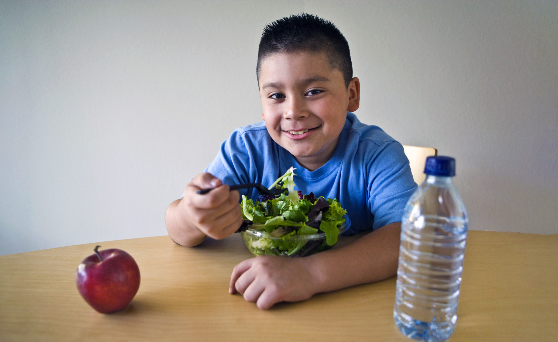 Pre-teen (10-12) boy sitting at desk and eating salad
