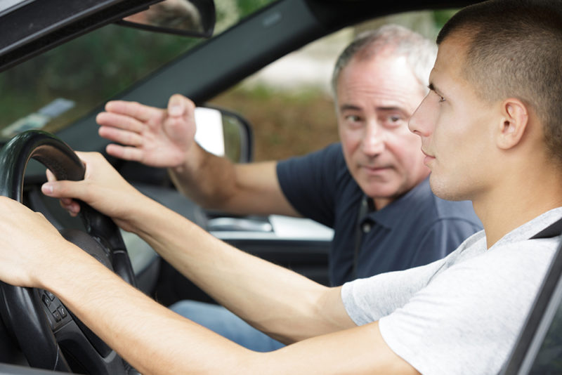 driving instructor gesturing to young adult learning to drive