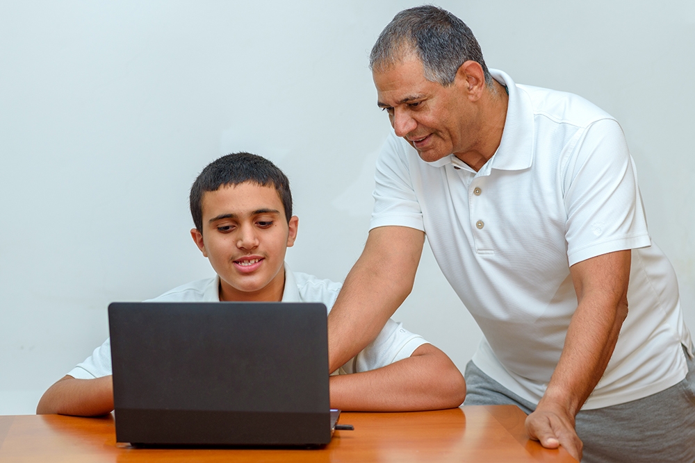 Senior Father and teenage son using laptop. Boy and dad sitting at home working with tablet computer.Happy family old grandfather and grandson on laptop.Elderly teacher trainer and teen pupil boy.