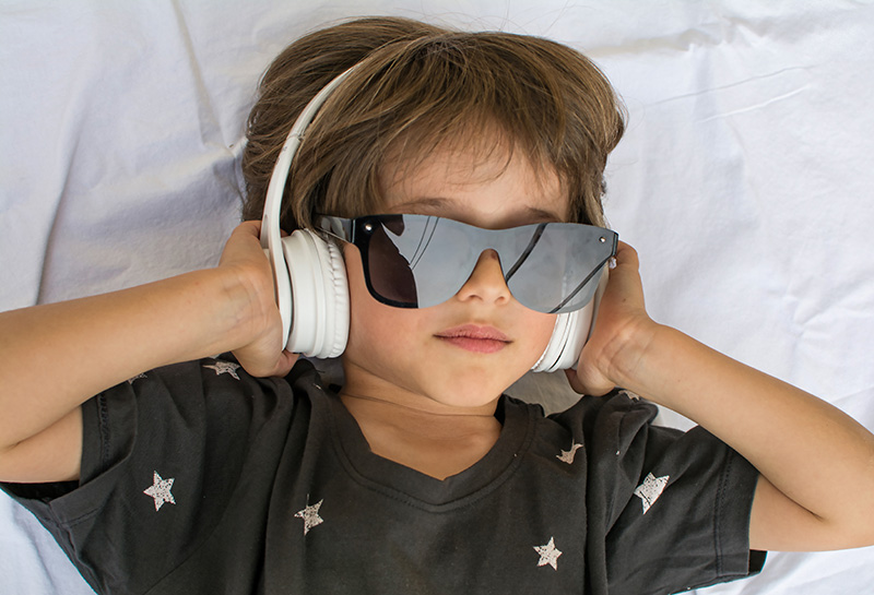 child blocking out sound and light with headphones and dark sunglasses