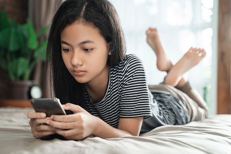 teenage girl using mobile smart phone at home while laying on the bed
