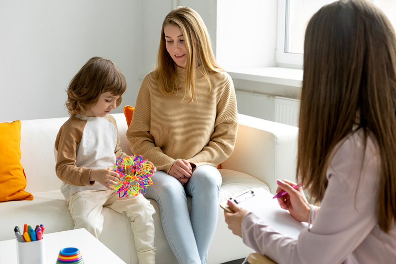 young girl playing with a toy on a couch with her mother getting an autism diagnosis