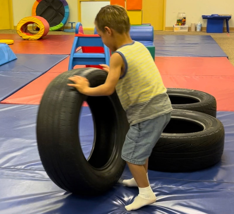 A child demonstrates an example of heavy work to the proprioceptive system by lifting and flipping readily accessible repurposed tires