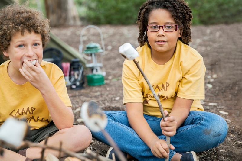 Two children at summer camp sitting around a campfire roasting marshmallows