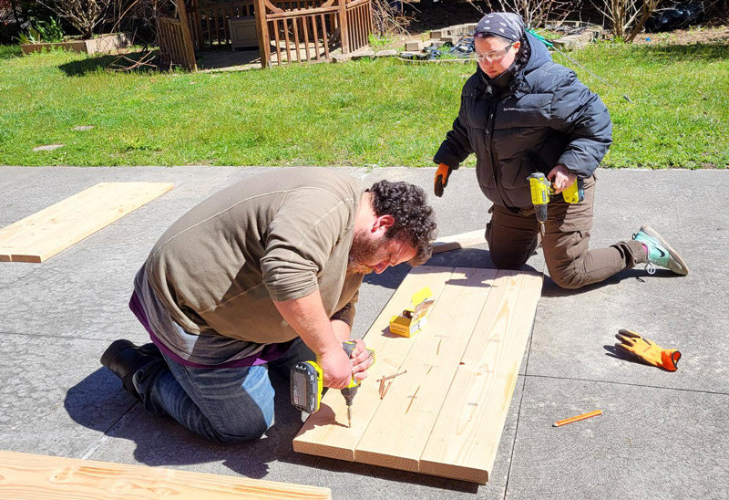 Urban farmer Noel (left) uses a power tool to build a raised bed with the help of a volunteer.