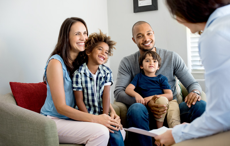Happy young family sitting on couch and talking with family counselor