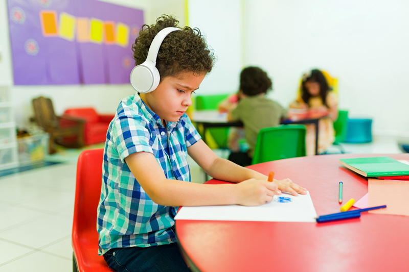 preschooler with headphones coloring alone in class