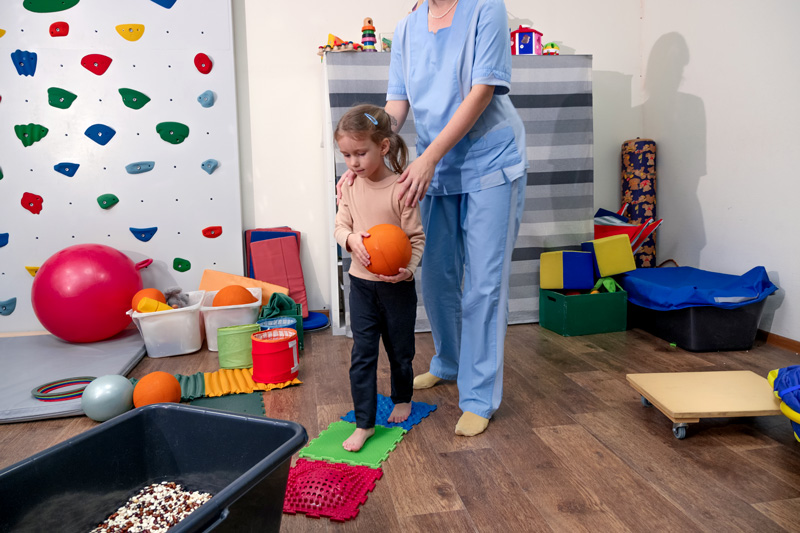 A child learning how to control sensory behaviors with an occupational therapist and ball