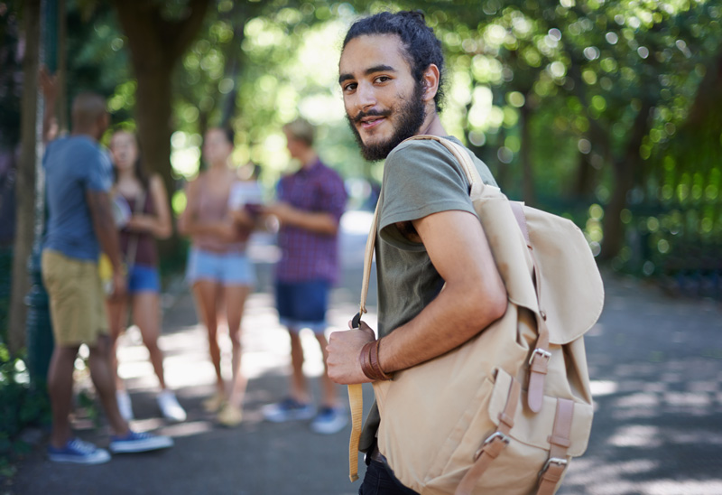 Young man with a backpack looking back at the camera with friends in the background