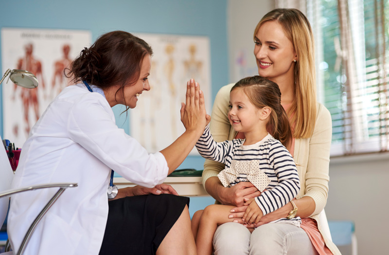 Mother and daughter smiling with doctor during health care visit