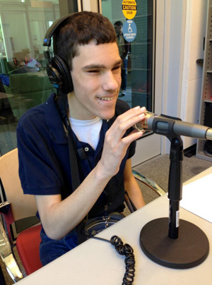 A Perkins student smiles as he uses a microphone to record a podcast