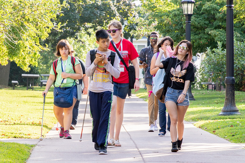 A group of Perkins School for the Blind teenagers walk across a sunny campus together