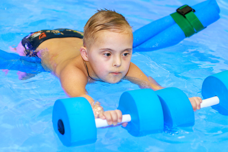 Young disabled boy swimming in a pool with floaties