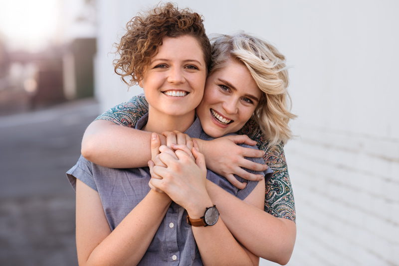 Portrait of a smiling young lesbian couple hugging each other while standing together on a city street