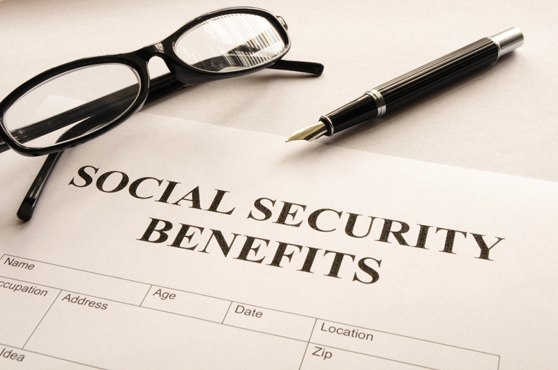  A pair of glasses and a pen rest on top of a document titled "Social Security Benefits," with fields for personal information visible at the bottom.