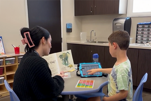 Engaged in the story, this boy uses his communication device to answer question s and share his thoughts, bringing the tale to life with his comments.