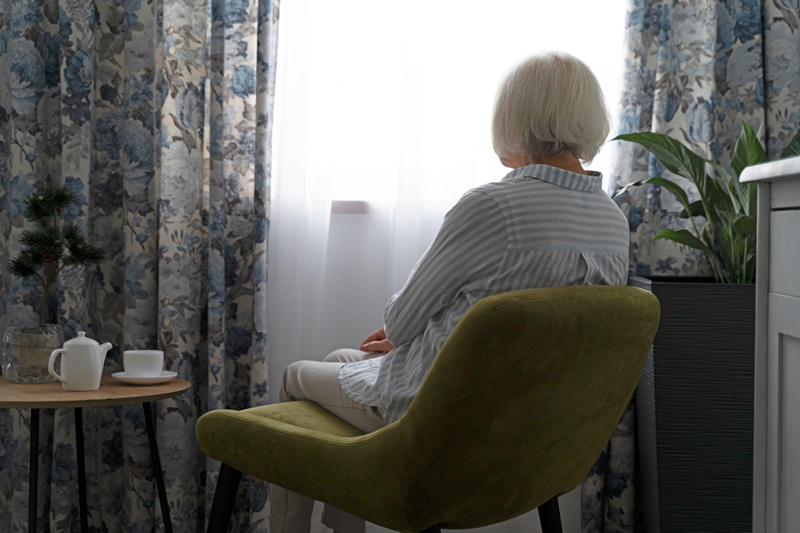 Lonely elderly woman looking through a window