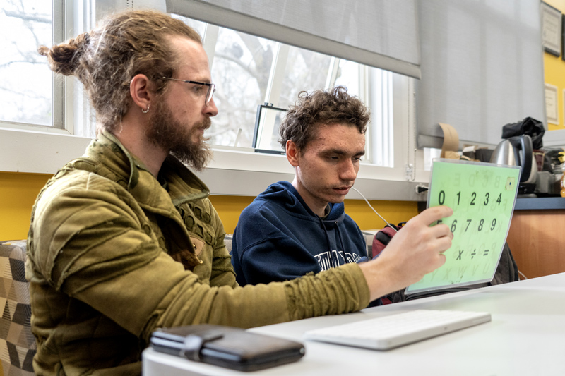 Noah McSweeney selects letters to ask a question of a guest speaker with the help of his communication partner Buckminster Barrett during an Oak Leaf class March 4, 2025. Photo credit: Ziggy Leon Carrillo