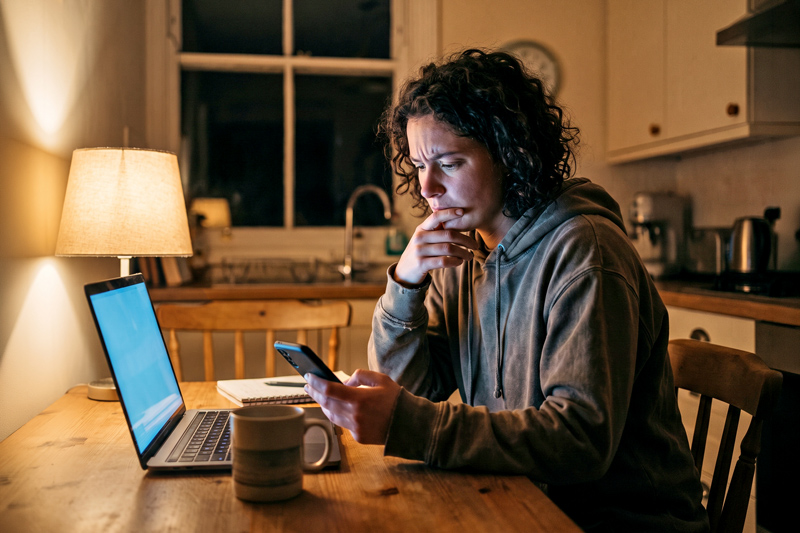 Young Adult at Night at Kitchen Table on Phone and Laptop